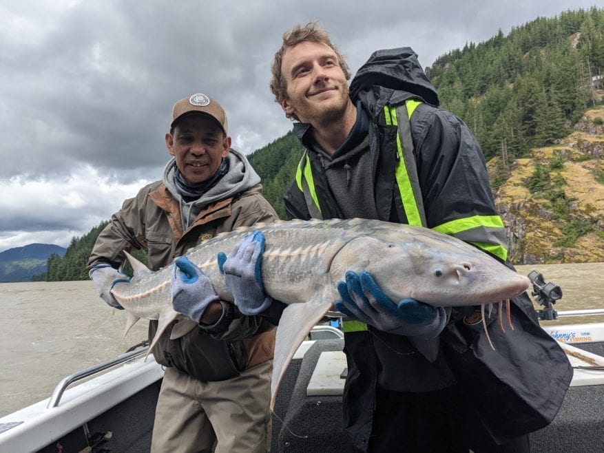 Two guys hold up a sturgeon and take a picture